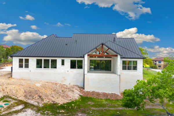 Rear elevation with hipped standing-seam metal roof, limestone walls, and cedar-trussed covered patio