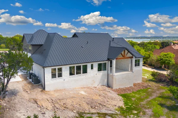 Aerial of a custom home with charcoal metal roof and distant lake views across the Texas Hill Country horizon