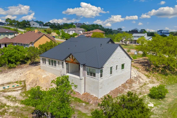 Aerial view of a new limestone home on a wooded hilltop lot in a Spring Branch TX custom home community