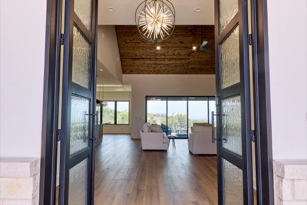 Custom iron double doors with rain glass open to a foyer with orb chandelier and vaulted wood-plank ceiling