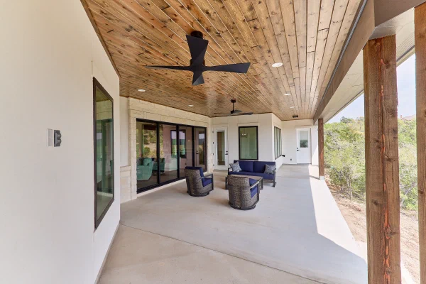 Deep covered porch with stained wood plank ceiling, black ceiling fans, and navy outdoor seating