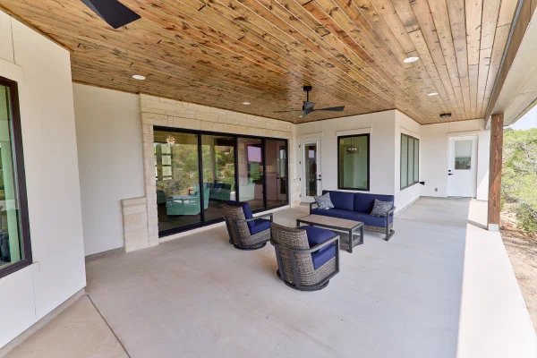 Covered patio lounge with navy cushioned wicker furniture beside a wall of black sliding glass doors