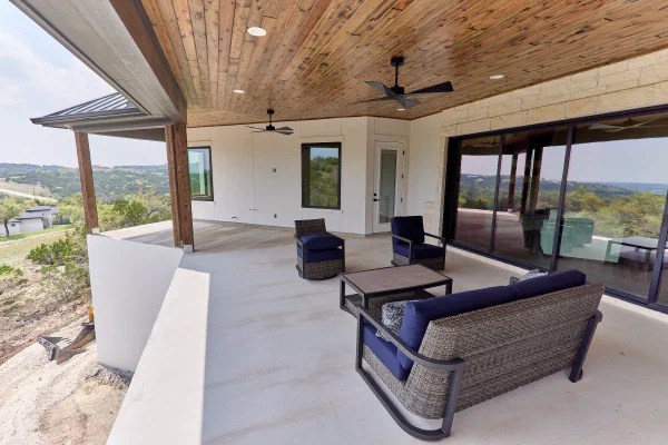 Wraparound covered porch with cedar posts and wicker seating overlooking rolling Texas Hill Country hills