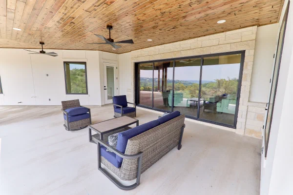 Expansive porch with limestone wall, sliding glass doors reflecting hillside views, and dual ceiling fans