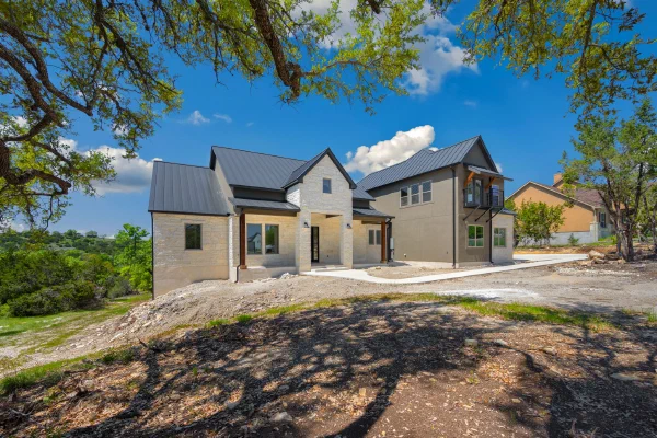Limestone and stucco custom home with black standing-seam metal roof framed by oaks on a Texas Hill Country lot