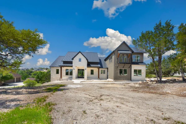 Modern farmhouse elevation pairing white limestone, taupe stucco, gabled metal roof, and an upstairs balcony