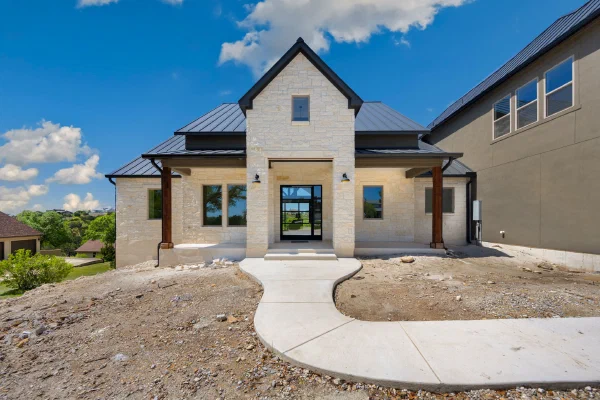 White limestone entry gable with cedar posts, black-framed glass front door, and standing-seam metal roof accents