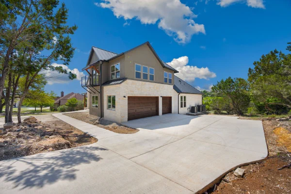Two-story custom home with limestone and stucco exterior, standing-seam metal roof, and three-car garage court