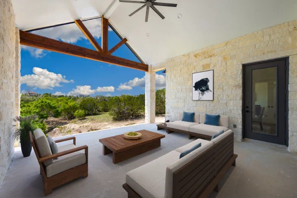 Vaulted covered patio with cedar truss, limestone walls, and outdoor seating overlooking Texas Hill Country views