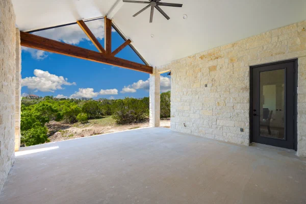 Covered back porch with vaulted ceiling, exposed cedar truss beams, limestone columns, and ceiling fan