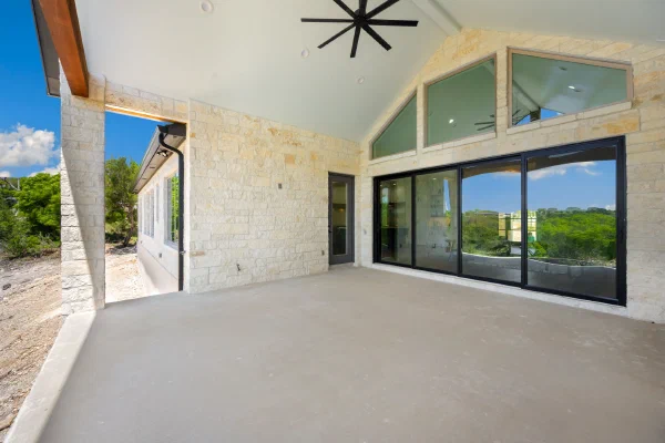 Limestone patio wall with black-framed sliding glass doors and gable transom windows opening to the back porch
