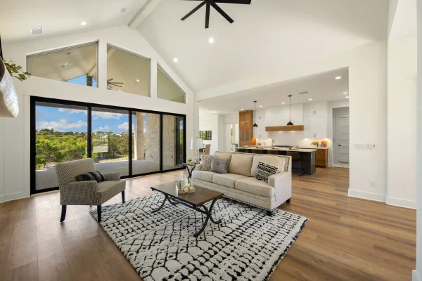 Open-concept living area under a vaulted ceiling with clerestory windows and sliding doors framing wooded hill views