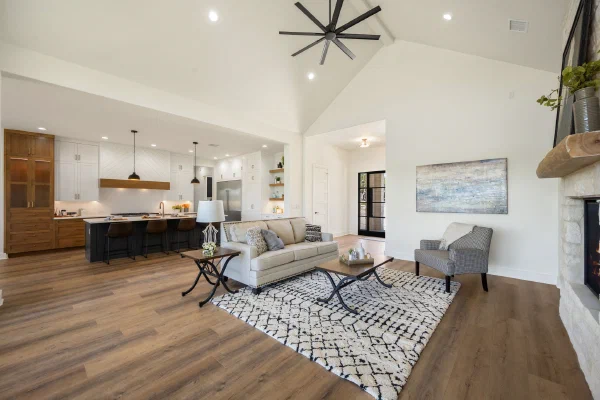 Open living room facing a kitchen with dark island, leather barstools, and wood-trimmed vent hood