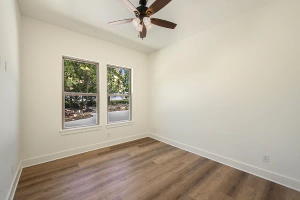 Bedroom with wood-look flooring, twin double-hung windows, and a dark-blade ceiling fan