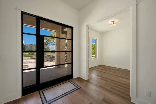 Entry foyer with black steel-framed glass front door and sidelight beside a sunlit study