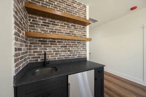 Wet bar detail with leathered black granite, matte black faucet, brick backsplash, and floating cherry shelves