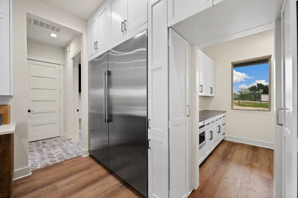 Butler's pantry with built-in stainless refrigerator, white shaker cabinets, and brick-paved hallway beyond