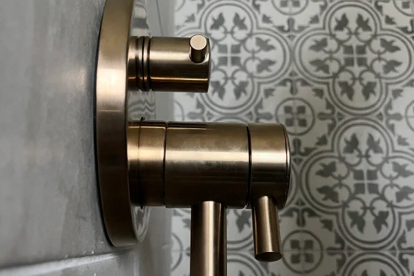Brushed brass shower valve detail against gray marble-look tile and a patterned accent wall