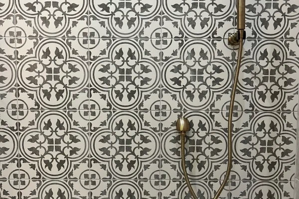 Shower wall in gray-and-white patterned tile with a brushed brass handheld sprayer