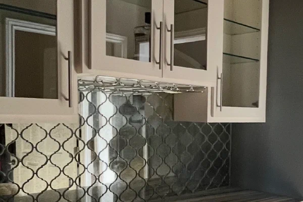 Bar with glass-front cabinets, mirrored arabesque tile backsplash, stemware rack, and dual wine refrigerators