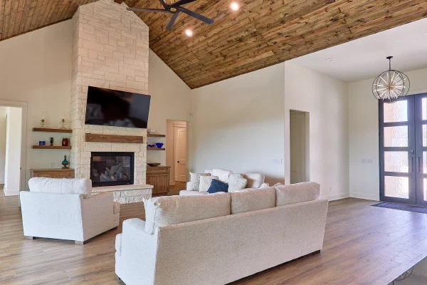 Vaulted tongue-and-groove wood ceiling rising over a full-height stone fireplace with rustic timber mantel