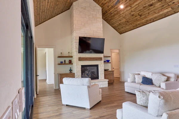 Cathedral wood ceiling with exposed beam over a limestone fireplace flanked by floating shelves in a custom home