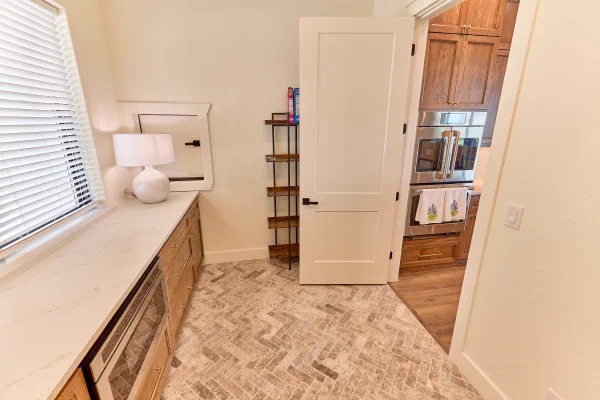 Butler's pantry with beverage cooler and quartz counters opening to a kitchen with stainless double ovens