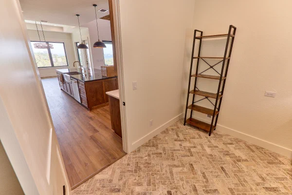 Pantry hall with herringbone tile floor beside an open custom home kitchen with island and pendant lighting