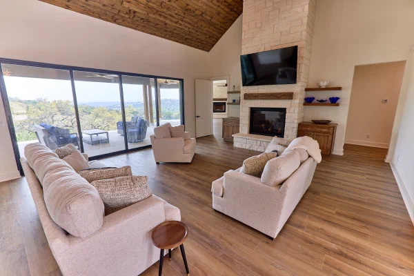 Living room with wood plank cathedral ceiling, limestone fireplace, and sliding glass wall to Texas Hill Country views