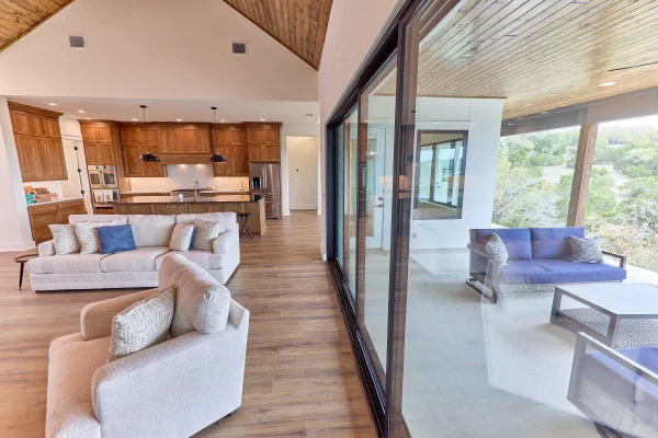 Multi-panel sliding glass door connects the great room to a covered outdoor lounge with wood plank ceiling
