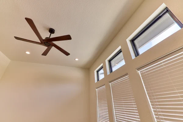 Walnut-blade ceiling fan and black-framed transom windows above white blinds in a light-filled bedroom