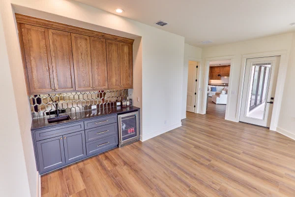 Wet bar with mirrored hexagon tile backsplash, black quartz counter, navy cabinets, and glass-front drink fridge