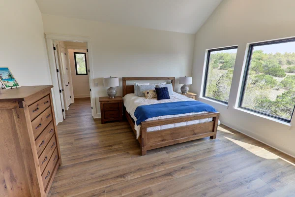 Primary suite with rustic oak bed and dressers, hill-view windows, and hallway to walk-in closet