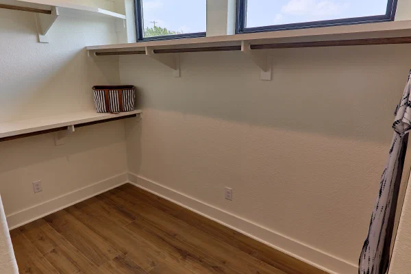 Walk-in closet with white built-in shelving, double hanging rods, transom windows, and wood-look flooring