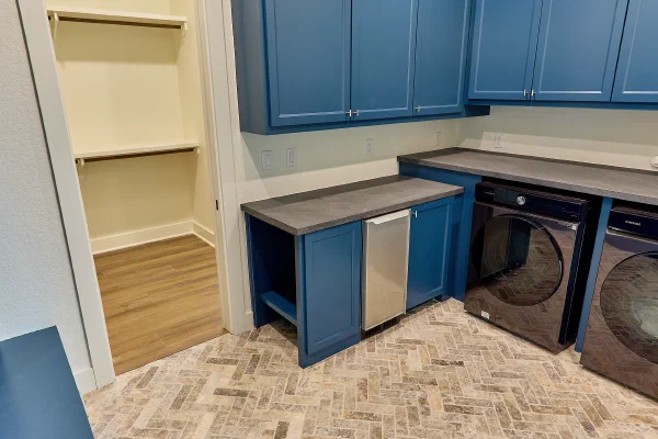 Laundry room with navy blue cabinetry, slate-gray counters, ice maker, and travertine herringbone brick floor