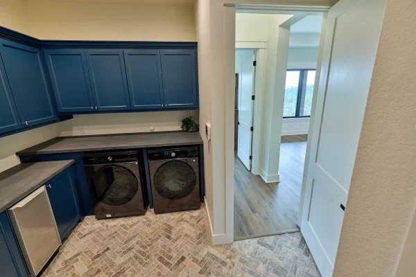 Laundry room with side-by-side front-load washer and dryer beneath deep blue cabinets and gray counters