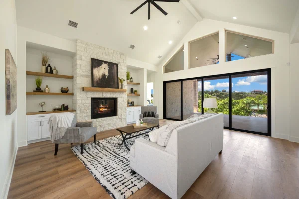 Vaulted great room in a Texas Hill Country custom home with limestone fireplace, cedar mantel, and sliding glass wall