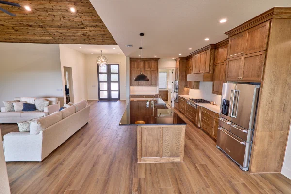 Vaulted wood ceiling and stone fireplace open to an oak kitchen with black granite island in the Texas Hill Country