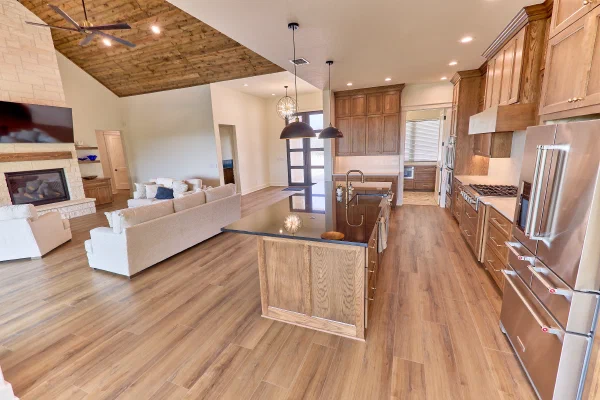 Oak kitchen with black granite island and copper accents opening to a vaulted living room with stone fireplace