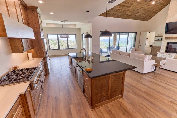 Oak kitchen with black granite island flowing into a living room with limestone fireplace and Texas Hill Country views