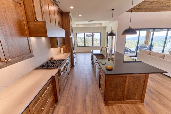 Galley kitchen with oak cabinets, quartz slab backsplash, gas cooktop and black island facing wall-to-wall windows
