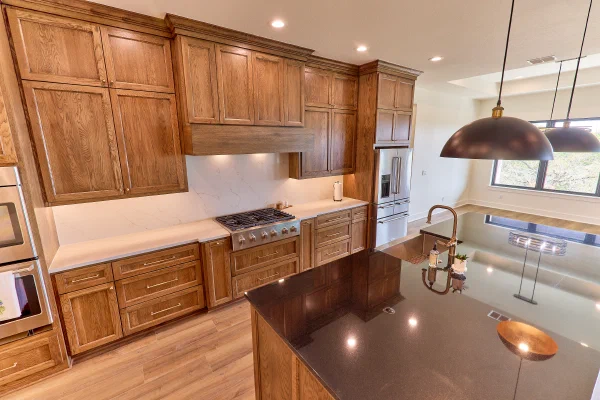 Oak upper cabinets and wood hood over a gas cooktop, with stainless refrigerator and polished black granite island