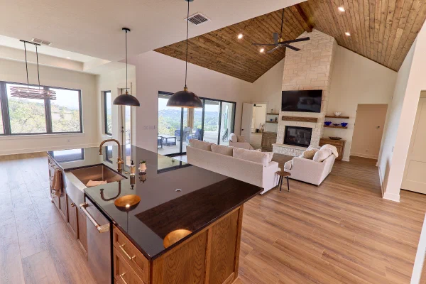 Custom home great room with plank ceiling, limestone fireplace and island with copper farmhouse sink and patio views