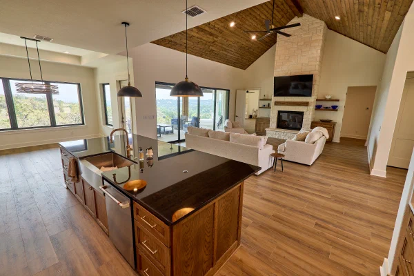 Copper farmhouse sink and brass faucet in a black granite island overlooking cream sofas and a limestone fireplace