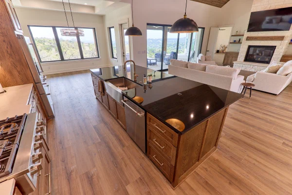 Black granite island with farmhouse sink and dishwasher facing bright windows with Texas Hill Country tree views