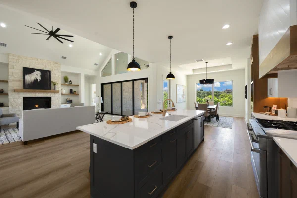 Black island with brass faucet opens to a stone fireplace living area in a Texas Hill Country custom home