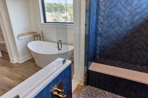 Navy herringbone tile shower with quartz bench, penny tile floor, and brass fixtures beside a freestanding tub