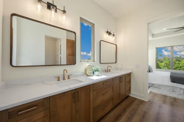 Primary bath double vanity with quartz counters, brass faucets, wood shaker cabinets, and black glass sconces