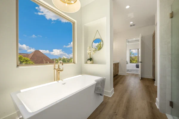 Freestanding soaking tub with brass floor-mount filler beneath a picture window framing Texas Hill Country views